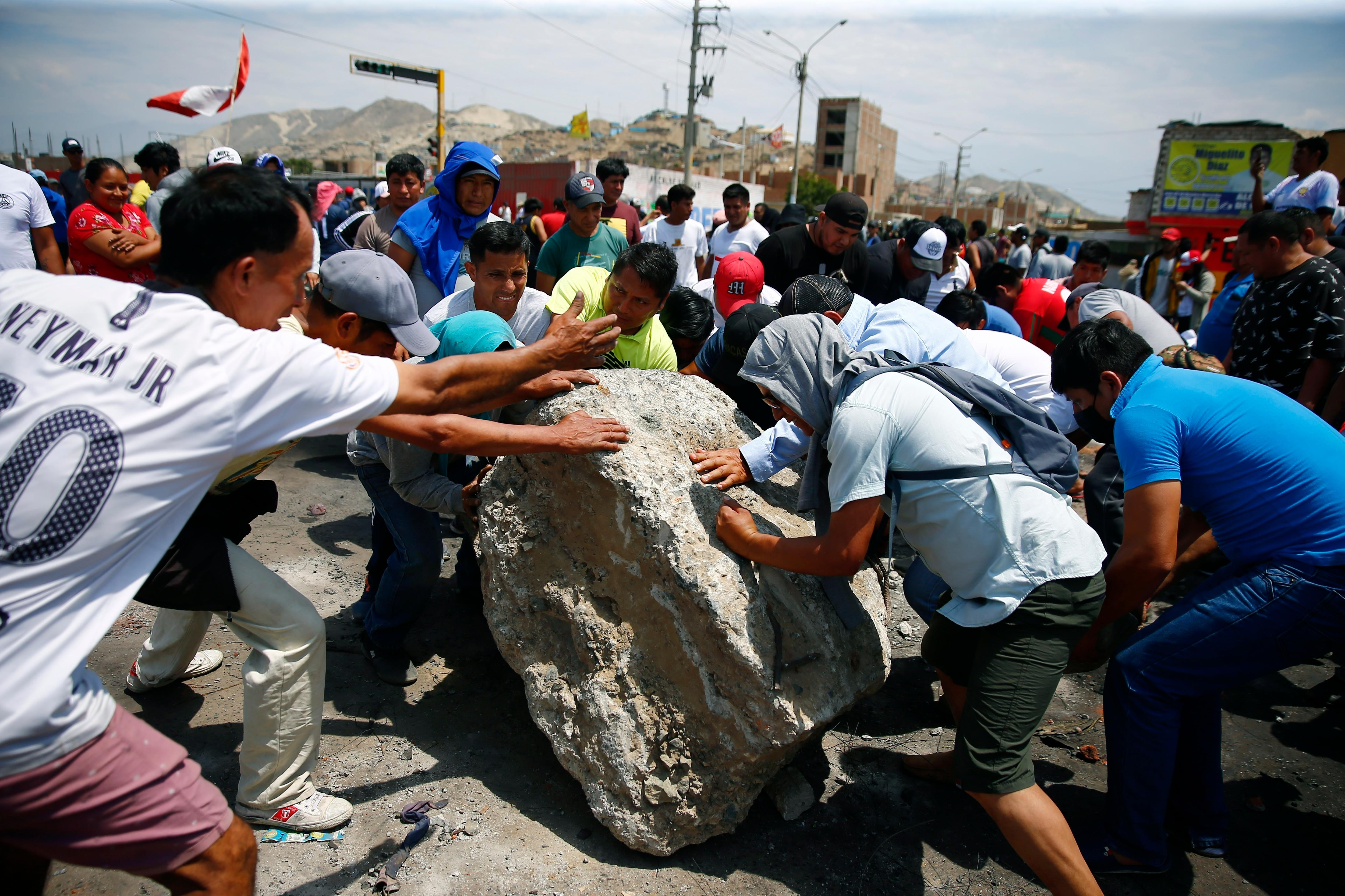 People work together to roll a boulder onto a highway during protests.