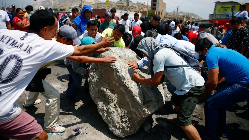 People work together to roll a boulder onto a highway during protests.