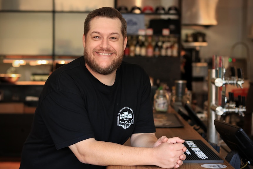 Daniel Chin sits at a bar, smiling and wearing a black t-shirt.