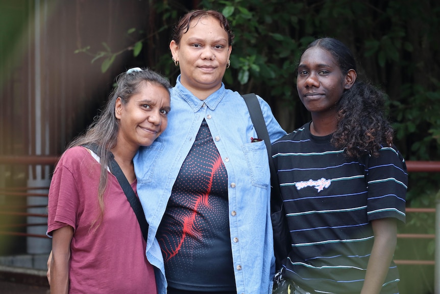 three Indigenous women standing side by side in front of Darwin Local court with green plants in the background
