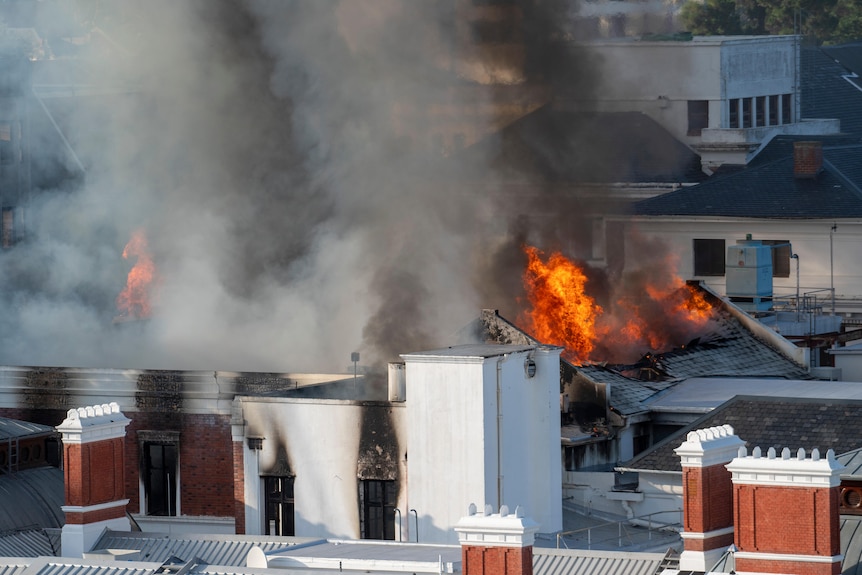 Пламя вспыхивает на крыше здания, дым поднимается над белыми трубами.