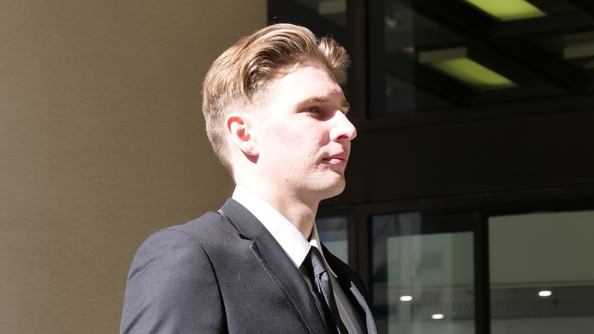 A young man in a suit walks out of court. He has short, reddish hair and is photographed from his right side.