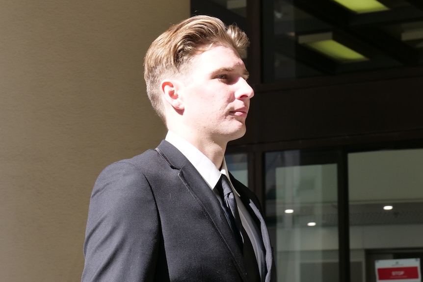 A young man in a suit walks out of court.