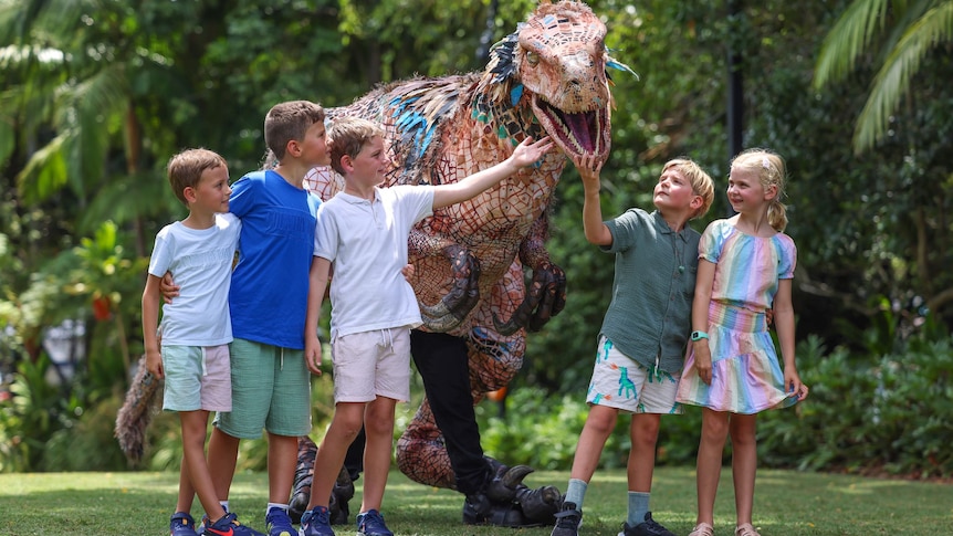 Five children playing with a dinosau.