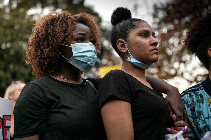 two black women, one wearing a mask