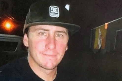 A young man in a black baseball cap and black T-shirt looking at the camera