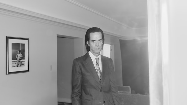 Man in suit stands in a brightly lit empty hallway with one picture hanging on the wall