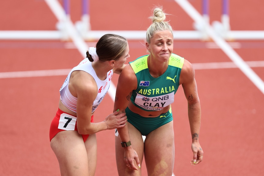 An Australian hurdler grimaces in pain as a fellow competitor holds her arm to check if she is ok. 