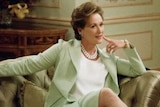 Meryl Streep sits on a chair with her finger pointed at her chin, thinking and smiling.