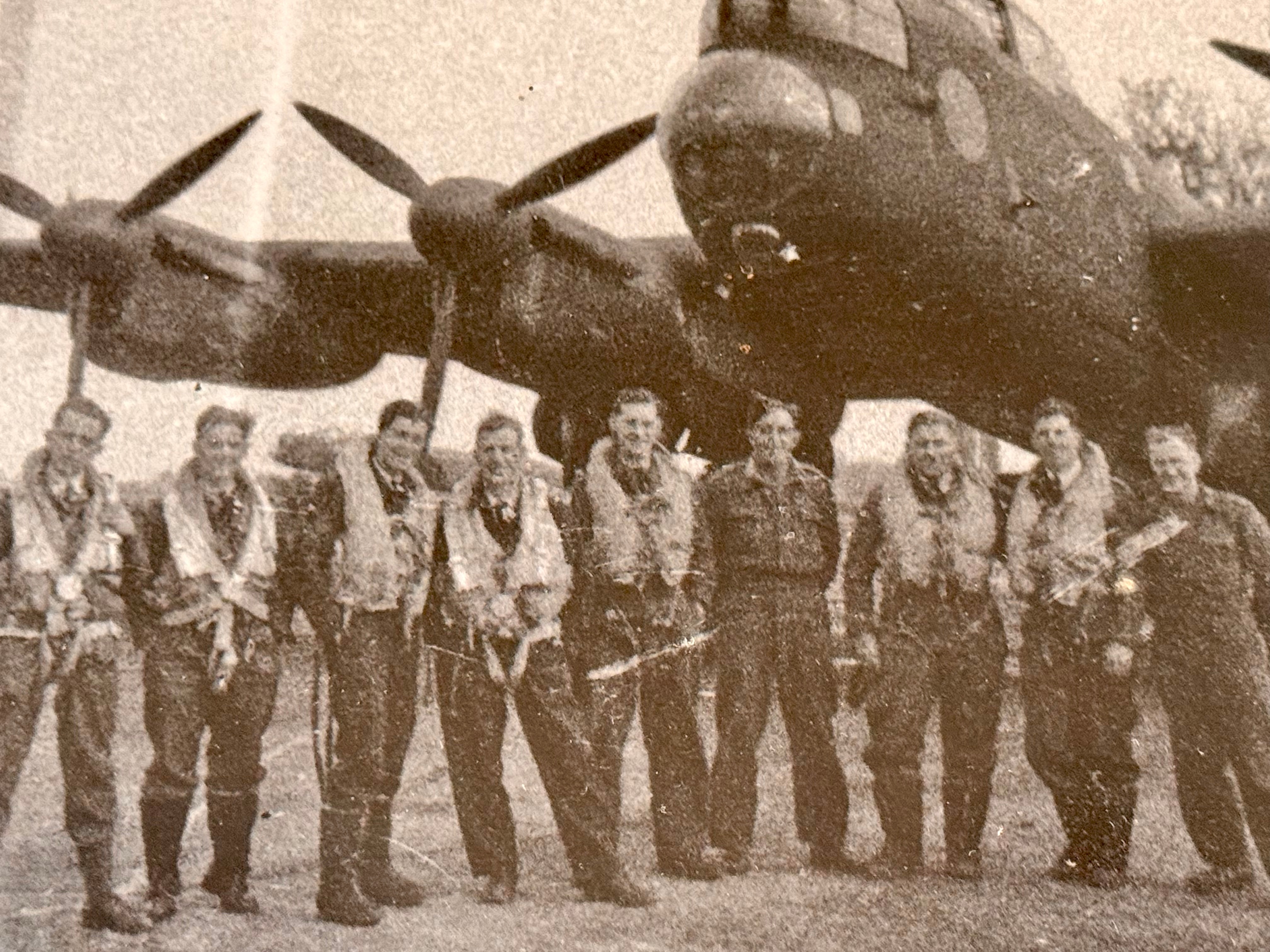 A group of men stand arms around each other in front of a large plane. 