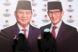 Two women dressed in black, full face veils stand in front of a large political banner in Indonesia.