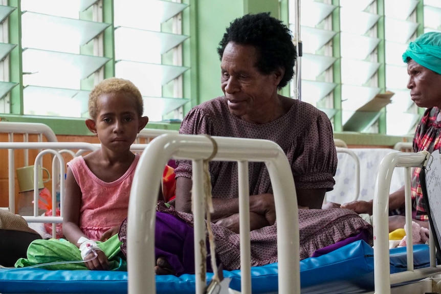 A woman and child sit on a bed together in a hospital ward