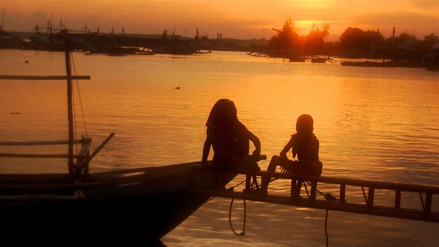 Two young boys stare out at the sunset over the bay in the Philippines.