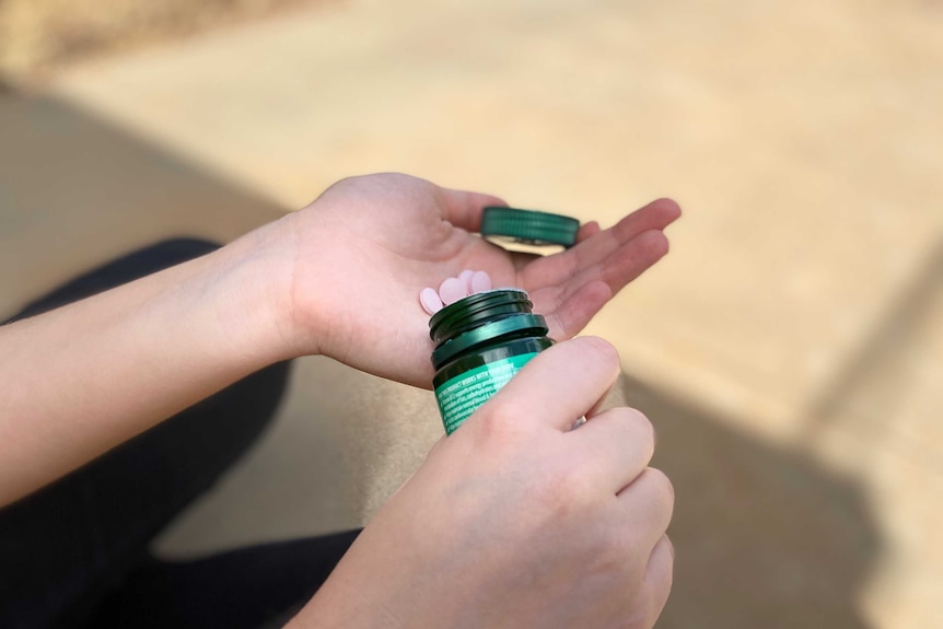 A woman shakes pills into the palm of her hand.