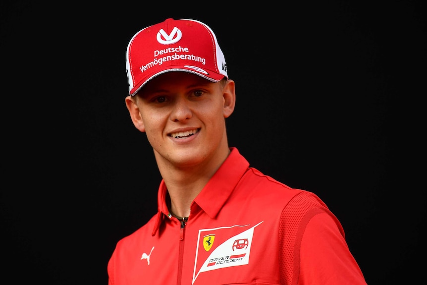 Mick Schumacher with a red cap and red shirt - and looking like his father - smiles at the camera.