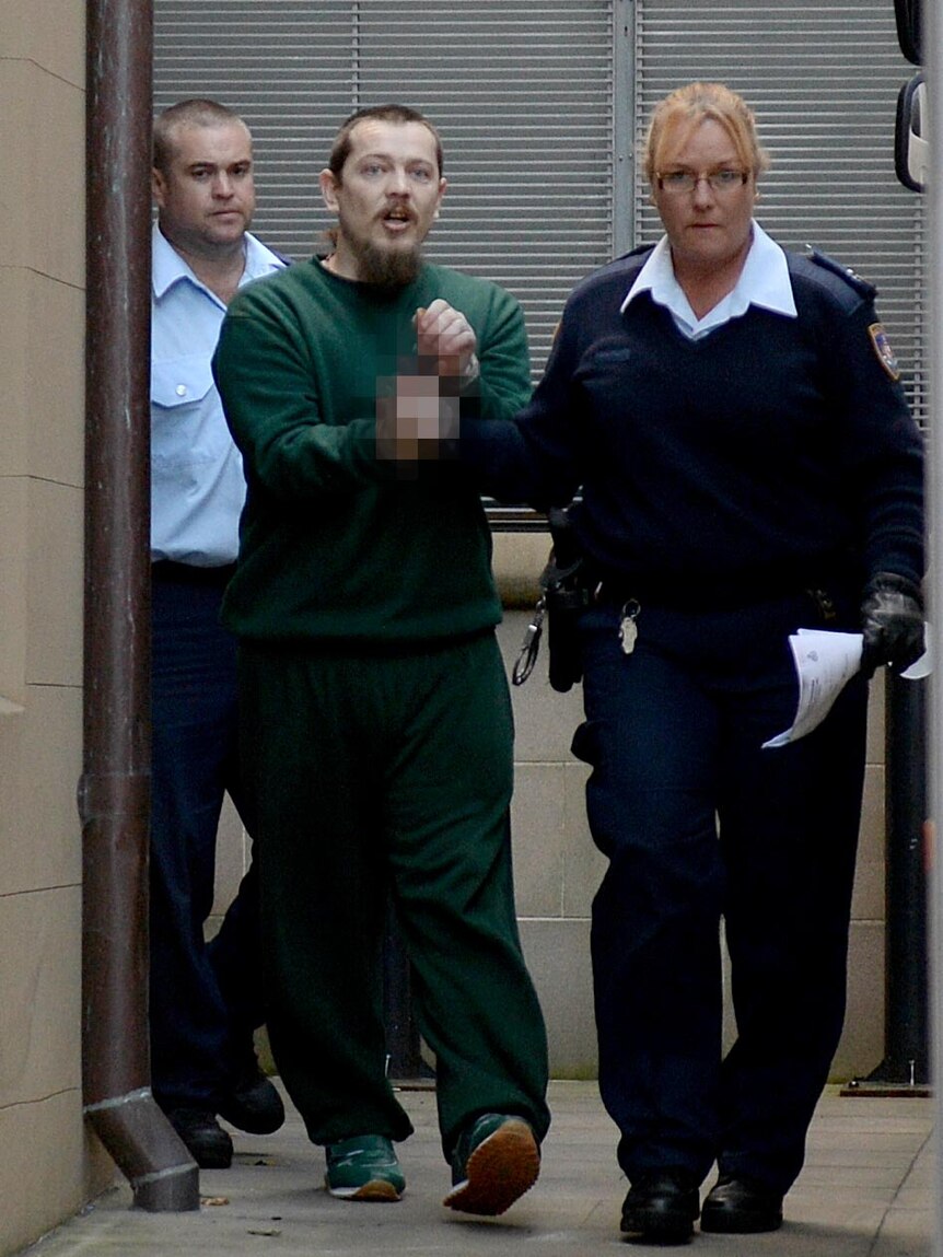 Warren Ross gestures to the media as he is escorted to a prison van at the NSW Supreme Court.