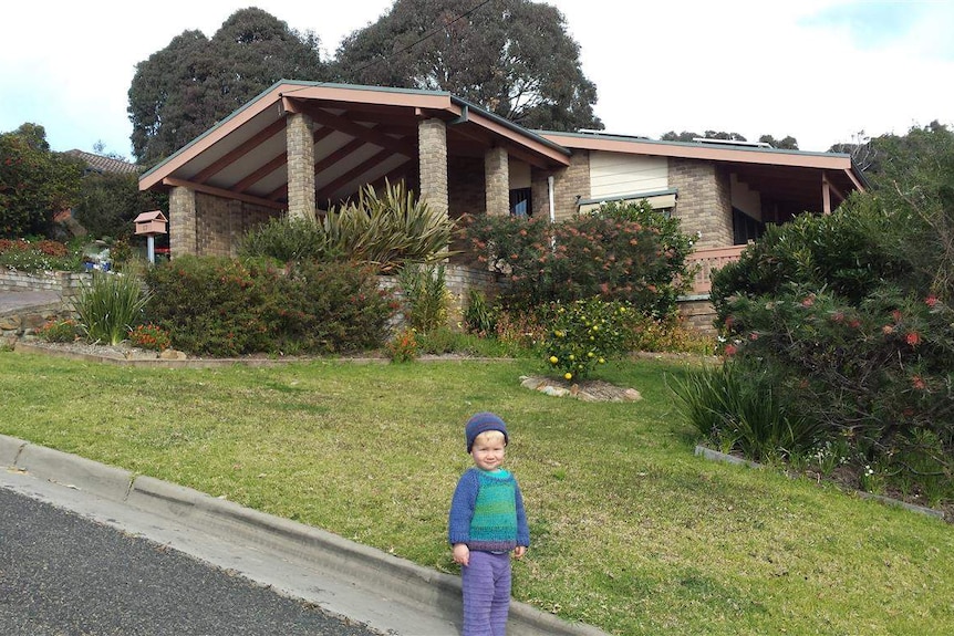 A young boy stands in front of a house.