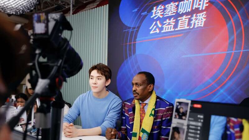 Un hombre chino se sienta junto a un hombre africano, ambos mirando a la cámara. 