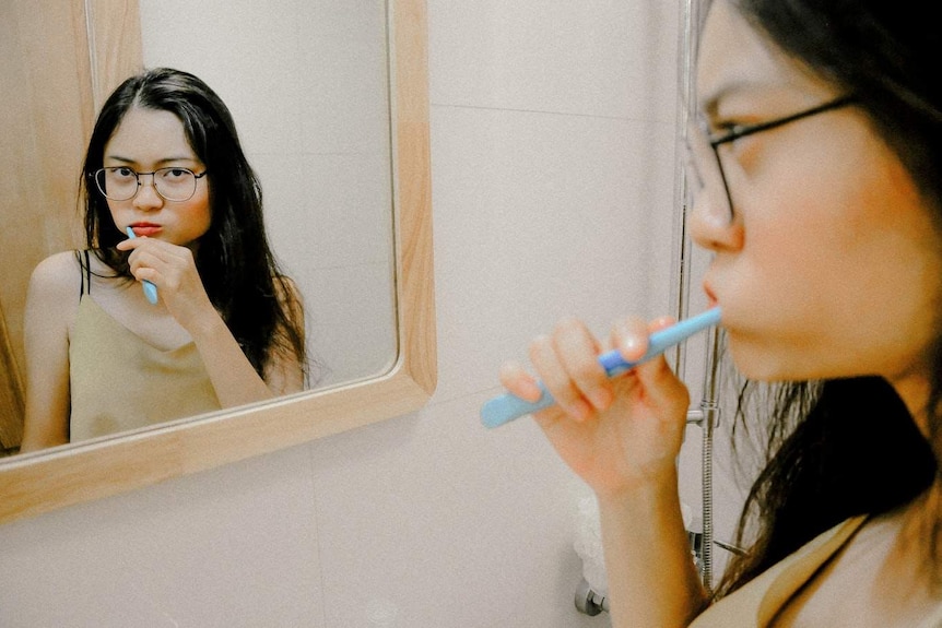 Woman looks at her reflection in the mirror while brushing her teeth.