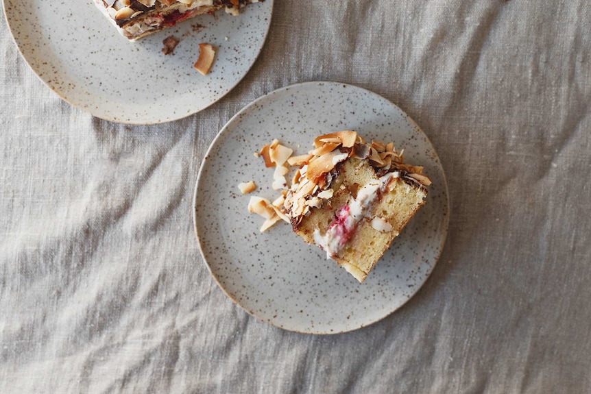 A slice of toasted coconut lamington cake on a plate on a linen table setting.