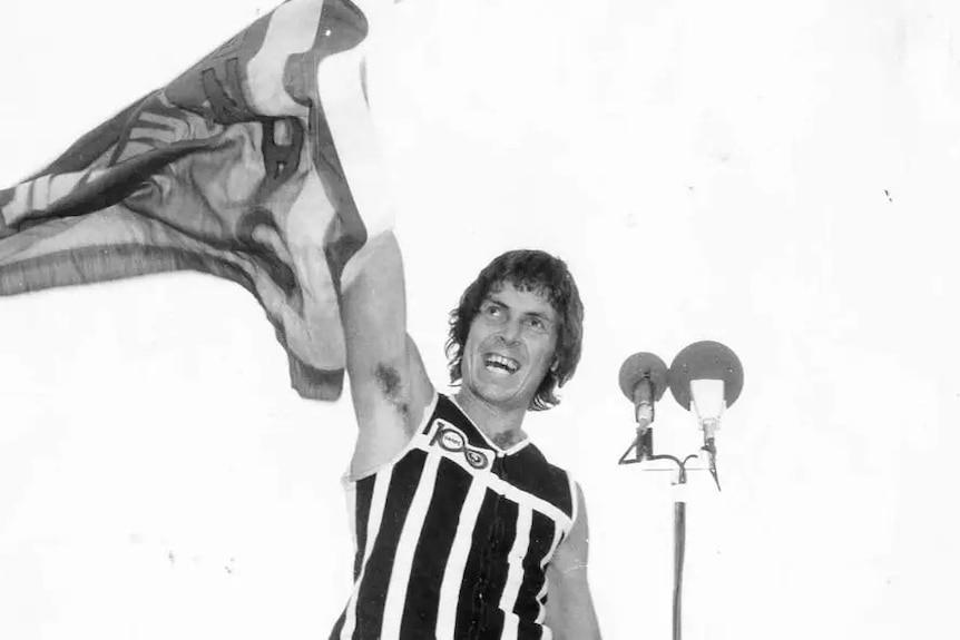 Foto hitam putih pemain Aussie Rules memegang bendera penuh kemenangan