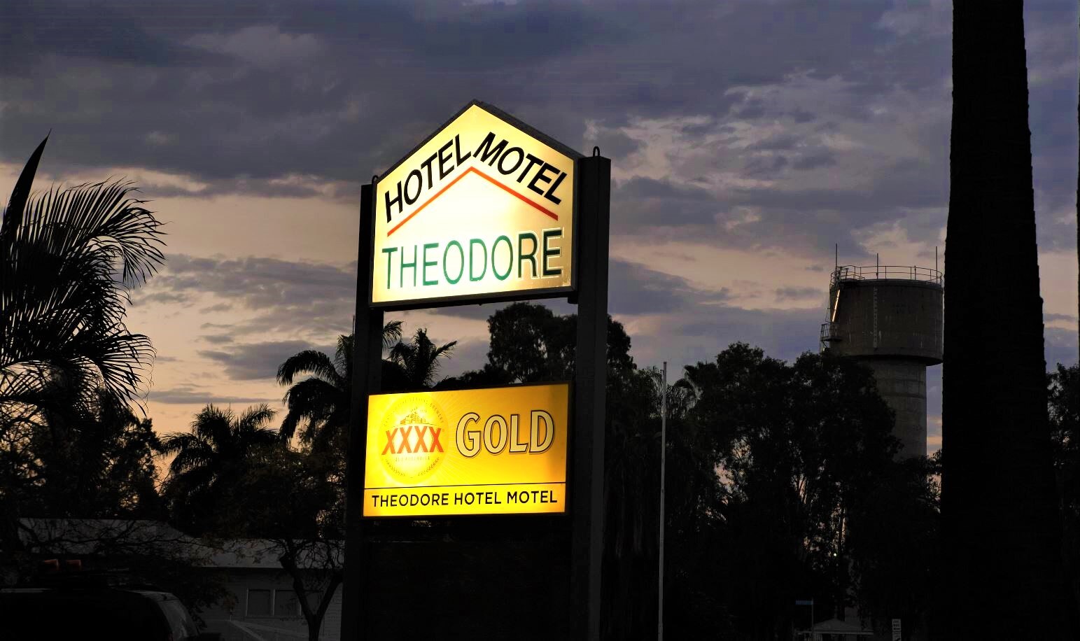 A sign saying Hotel Motel Theodore XXXX Gold Theodore Hotel Motel is illuminated against a night sky.