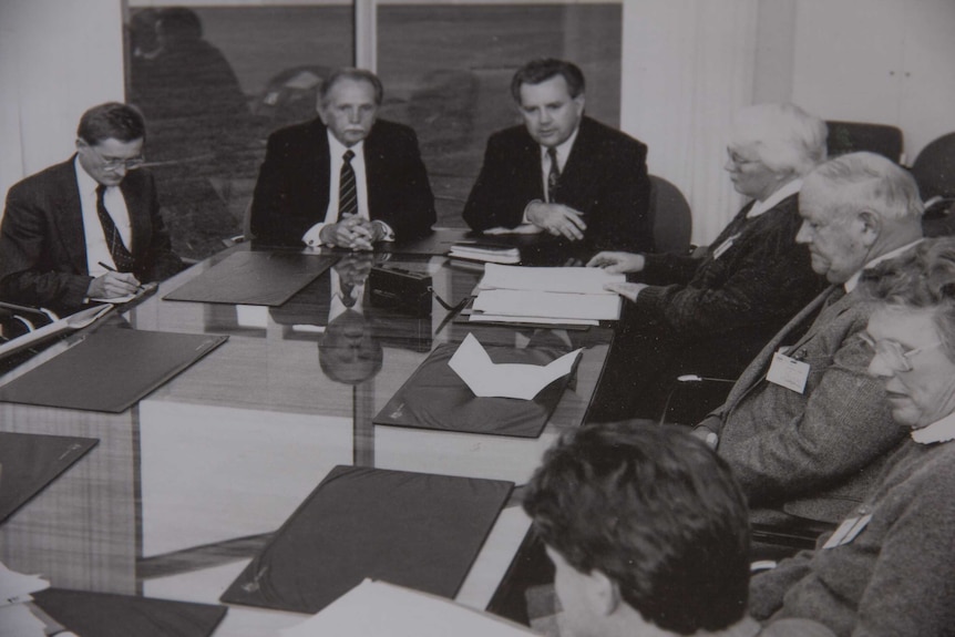 A black and white photograph of people sitting around a board room style table