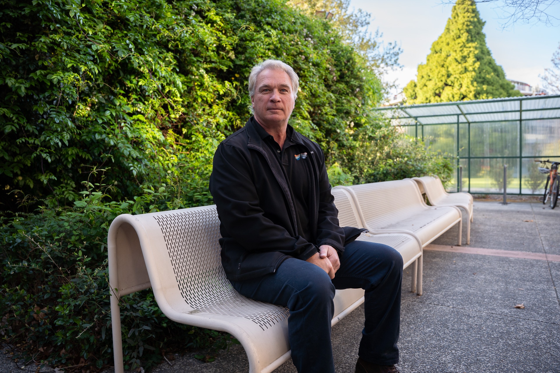 A man sits in front of a hedge.