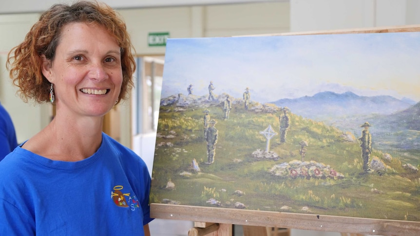 A woman stands smiling next to a painting showing an army service.