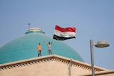 Two men hold the Iraqi flag on the roof of a government building in Baghdad.