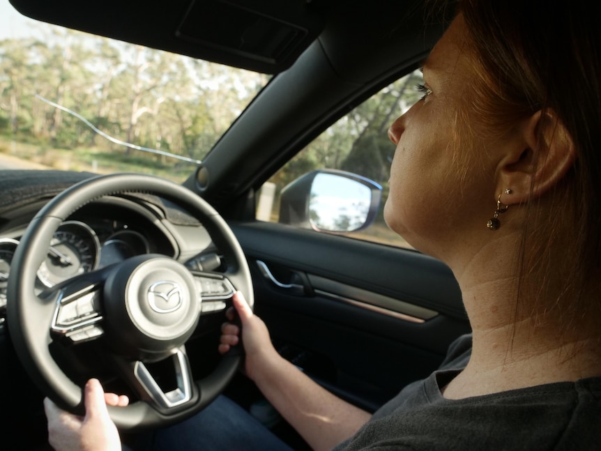 Profile of a woman with eyes on the road, driving through bushland.