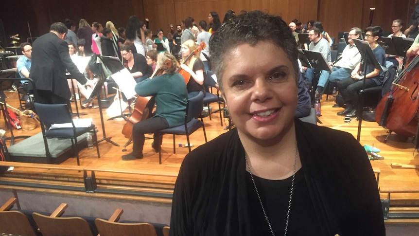 Deborah Cheetham poses in the foreground while the orchestra rehearses.
