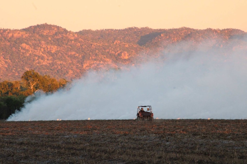 Farmers riding in a quad bike watch a small grass fire near the edge of their crops