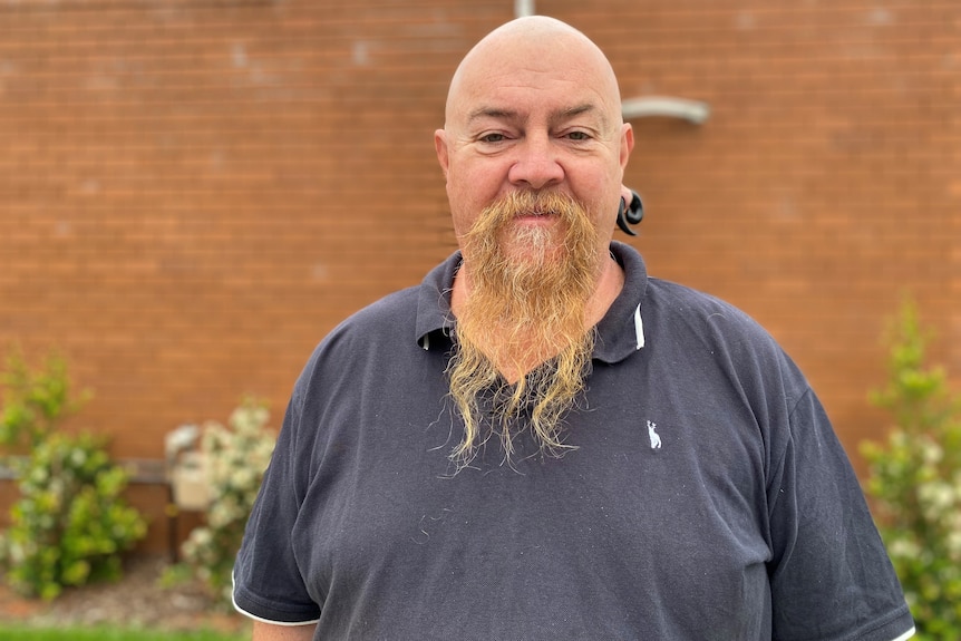 A burly man bald with a large wooden earring in right ear