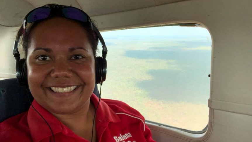 A woman wearing headphones smiles in a light plane next to a window