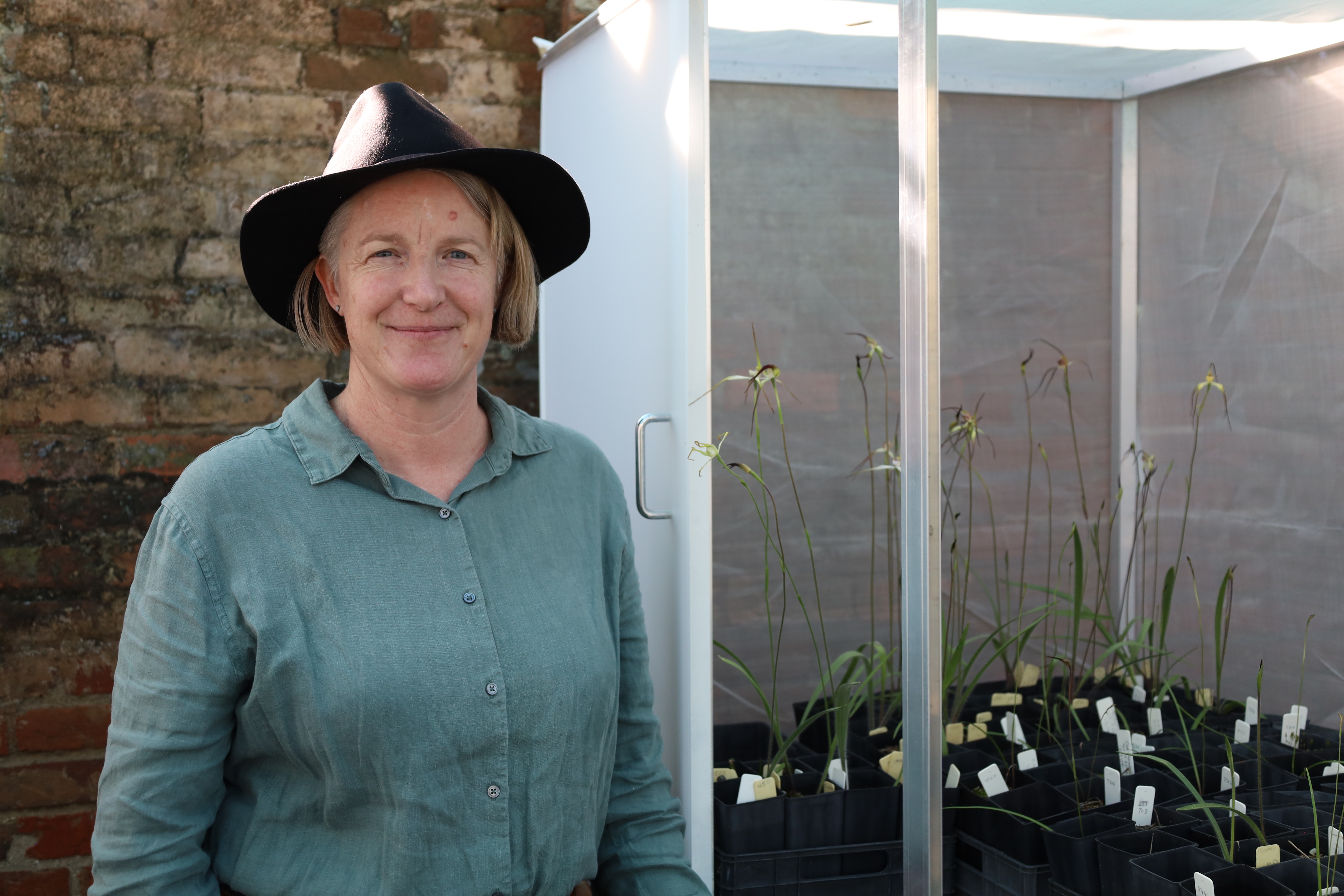Magali Wright stands near a collection of native Tasmanian spider orchids in pots.