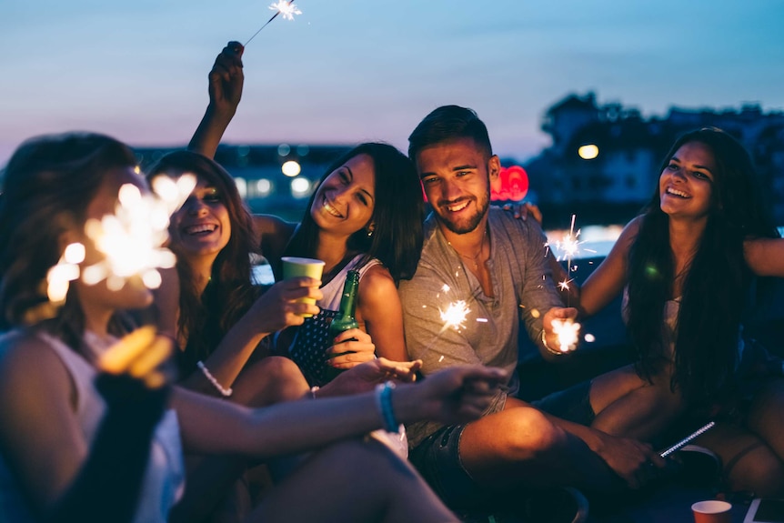 Happy friends partying on the rooftop with drinks and sparklers.