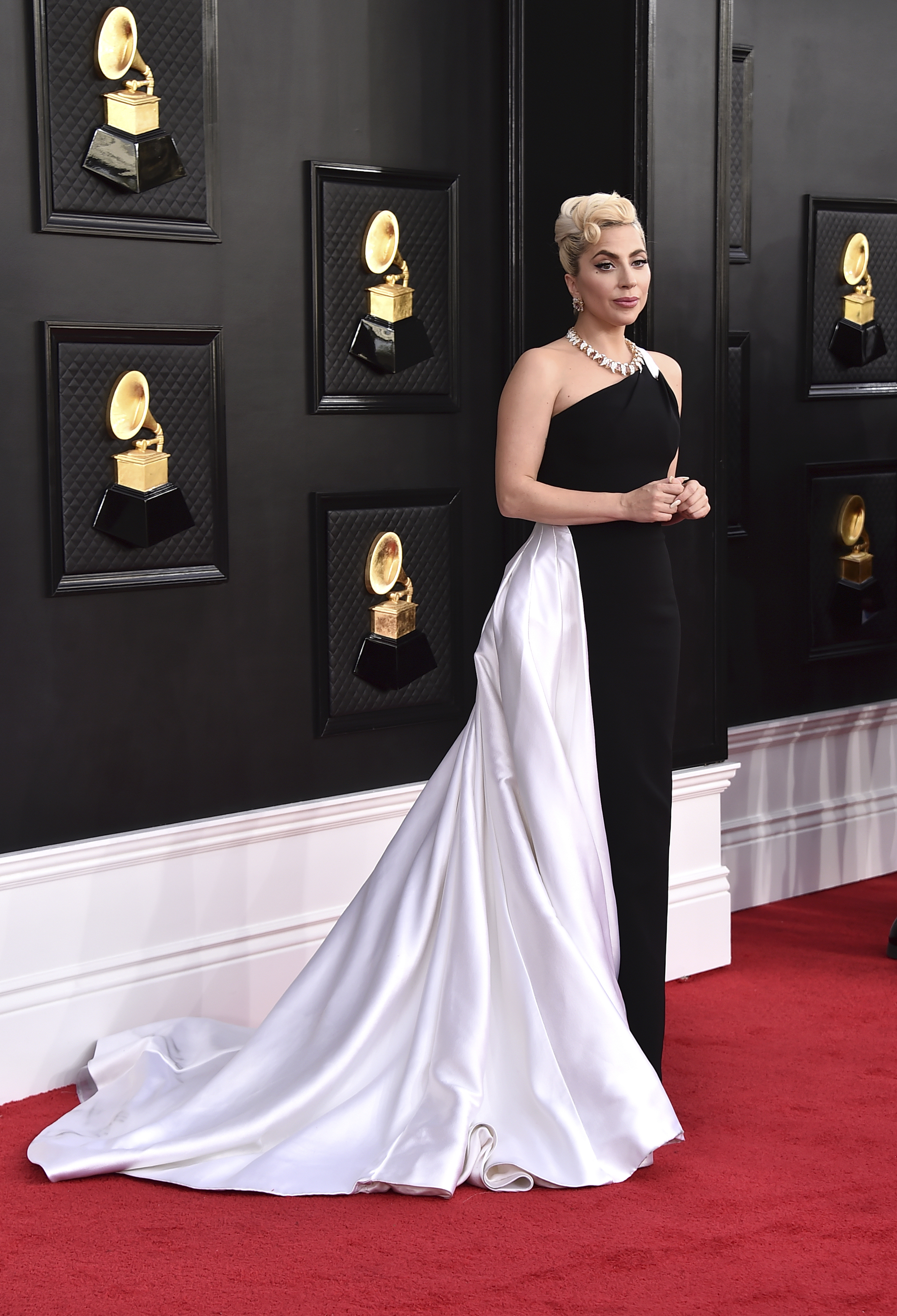 lady gaga stands on the grammys red carpet wearing a long black gown with a white bustle train