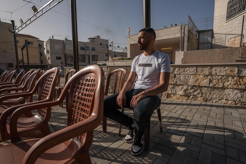 A young Middle Eastern man sits on a chair on a rooftop 