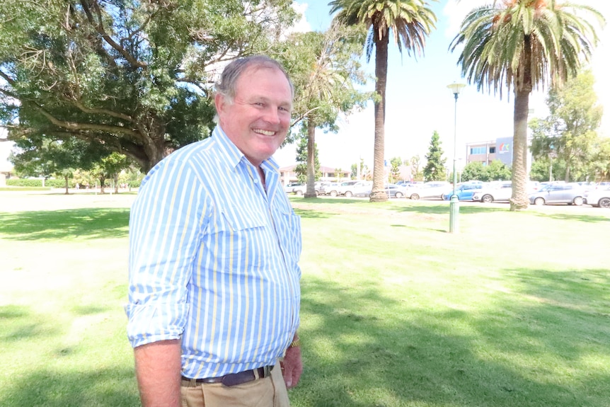 Man in blue and white striped shirt stands in a park. 