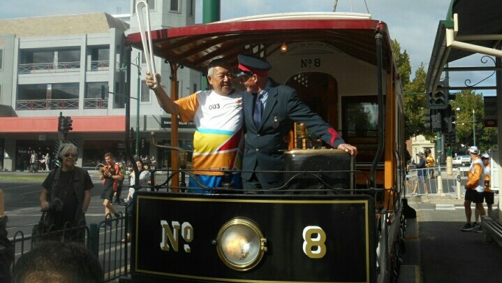 A man holding the Commonwealth Games Queen's Baton rides a tram with a conductor in Bendigo