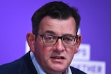 A bespectacled middle aged man with dark hair looks toward the camera as he speaks.