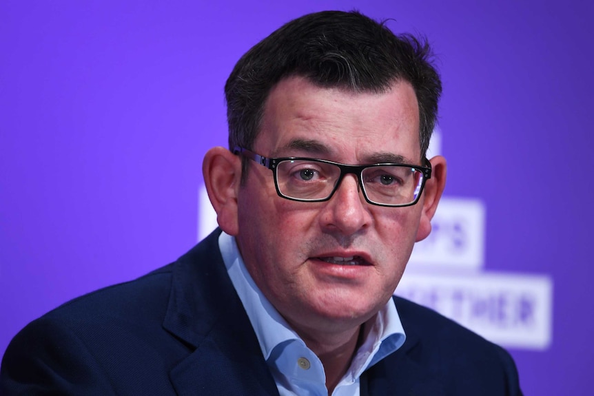 A bespectacled middle aged man with dark hair looks toward the camera as he speaks.