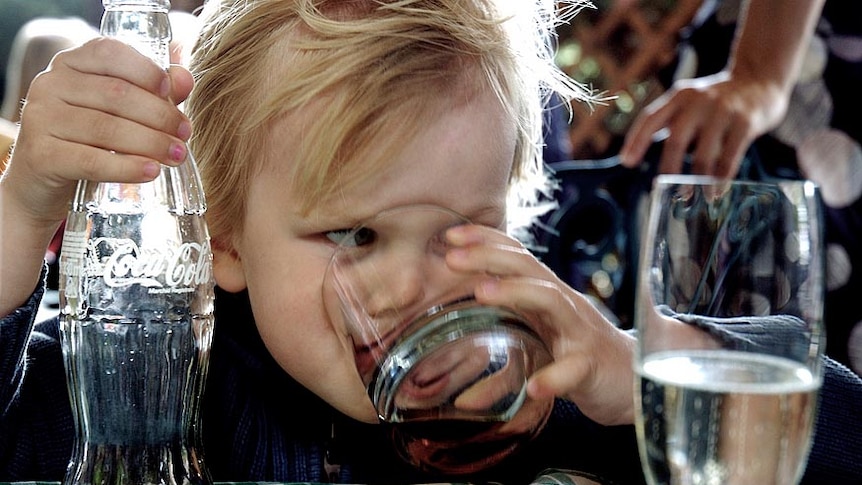 File photo of a young child drinking coca-cola from a glass, coke bottle in hand.