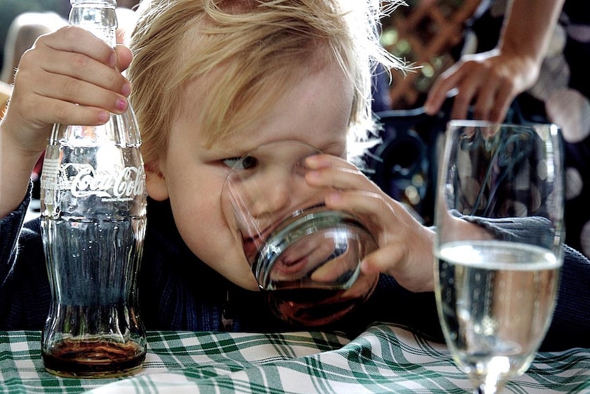 File photo of a young child drinking coca-cola from a glass, coke bottle in hand.