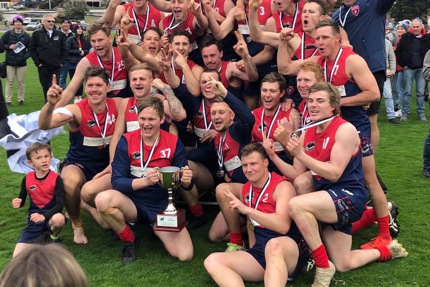Team mates at the Lilydale Demons gather round a premiership trophy. 