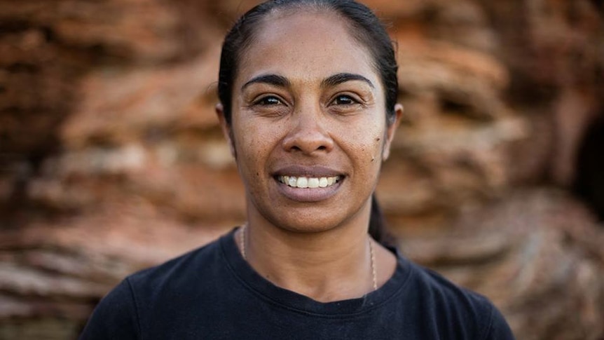 Portrait of Dalisa Pigram, a young Aboriginal woman in a black tshirt with hair tied up smiling