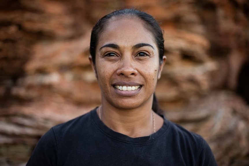 Portrait of Dalisa Pigram, a young Aboriginal woman in a black tshirt with hair tied up smiling