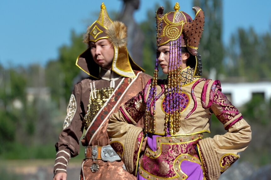 Two members of a Russian folk dance troupe, dressed in colorful costumes, stand with their hands on their hips. 