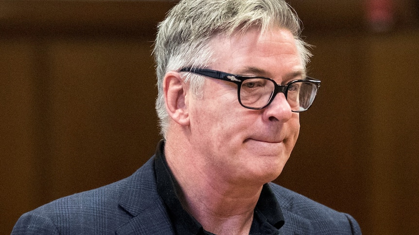 Actor Alec Baldwin purses his lips. He is wearing glasses. 